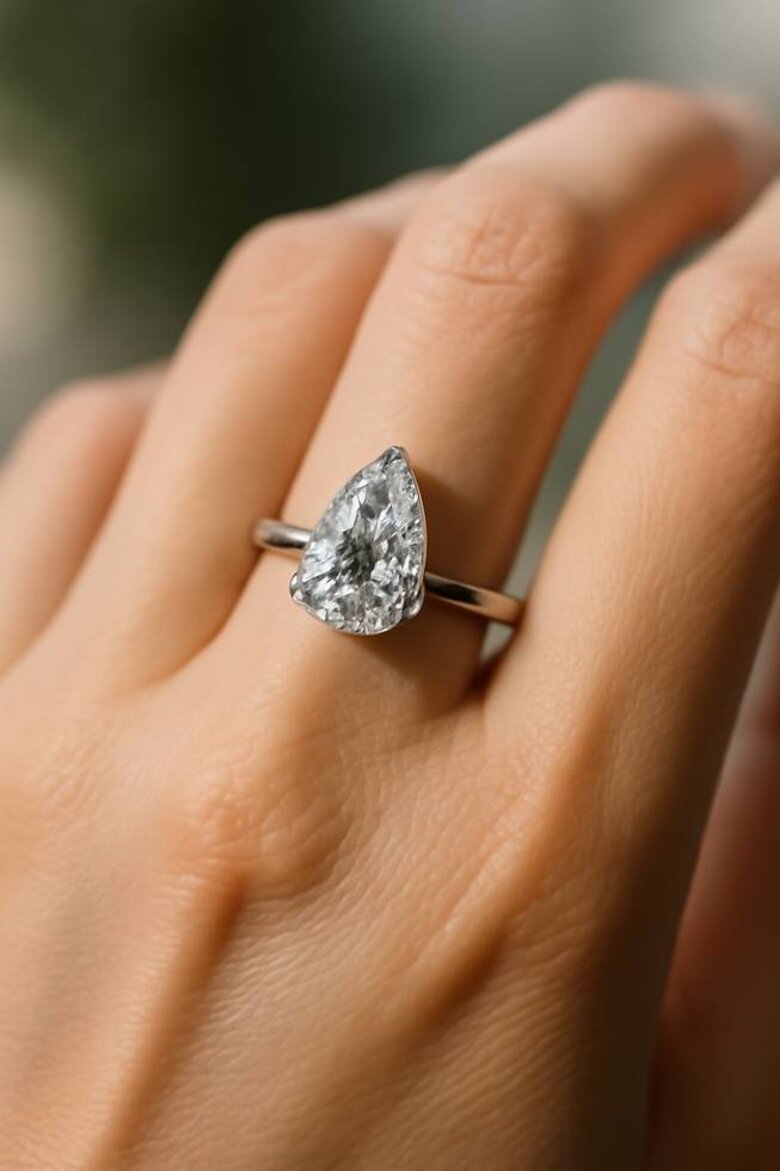 Image: Elegant Pear Lab-Grown Diamond Engagement Ring on Hand - Showcasing the teardrop silhouette in a platinum solitaire setting with natural lighting, demonstrating finger-flattering proportions and brilliance to capture reader attention immediately